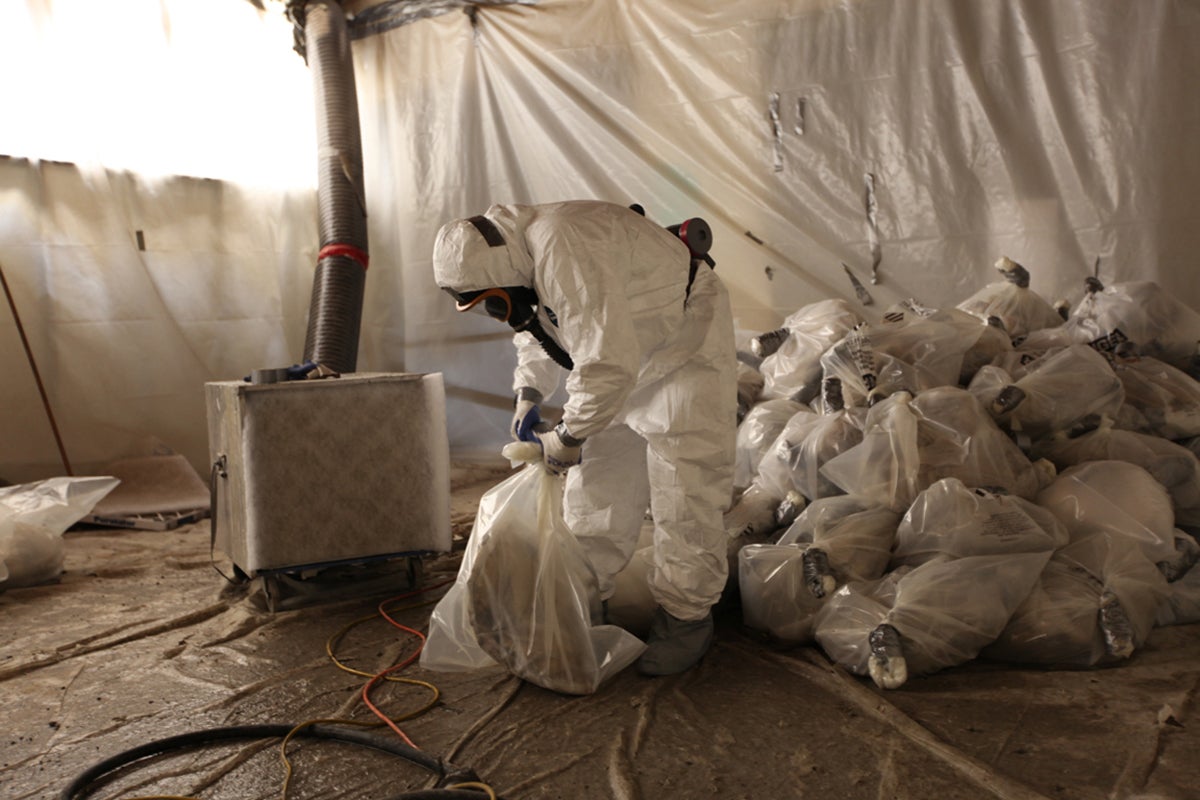 Worker in hazmat suit handling sealed bags.